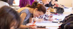 A group of people are at gathered at a workstation using stencils for creative projects.