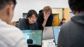 A goupr of RISD students are working on laptops at a white table. 