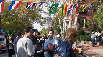 Students and guests gather at outdoor event with collection of national flags hanging overhead