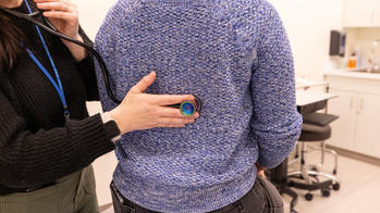A nurse is using a stethoscope to check the heartbeat of a patient in a blue sweater.