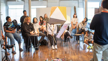 An undergraduate class of RISD students observe a piñata style artwork.