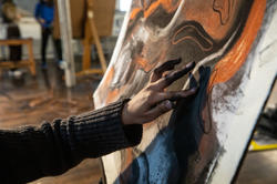 A RISD student's hand is reached out and hand-making a work of visual art.