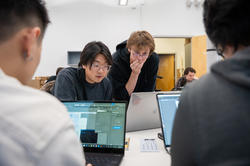 A goupr of RISD students are working on laptops at a white table. 