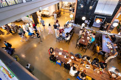 A bird's-eye view of people sitting at several long tables inside a dining hall.