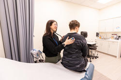 Clinician at RISD Health Services using stethoscope on patient.