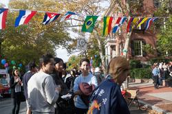 Students and guests gather at outdoor event with collection of national flags hanging overhead