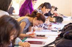 A group of people are at gathered at a workstation using stencils for creative projects.