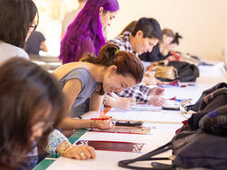 A group of people are at gathered at a workstation using stencils for creative projects.
